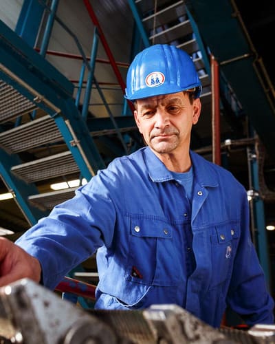 Mitarbeiter mit Schutzhelm an einer Maschine in der Werkshalle